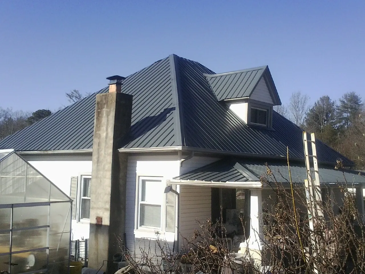 Dark blue standing seam metal roof on a white farmhouse with dormer — Slate & Tile Roof Repair by Roofing Brothers in Oyster Bay