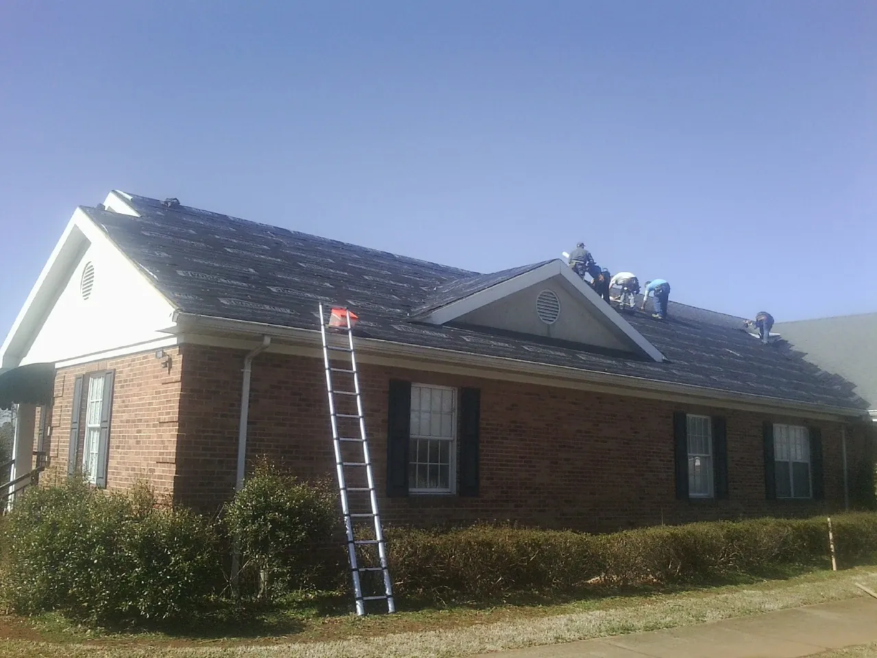 Crew tearing shingles off a brick ranch roof with a ladder set — Emergency Roof Repair work by our crew in Oyster Bay