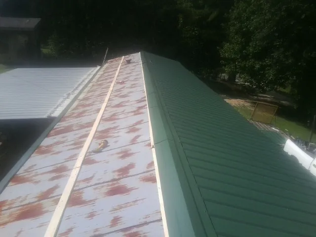 Old rusted panels beside newly installed green metal roofing — Wind Damage Roof Repair by Roofing Brothers in Oyster Bay