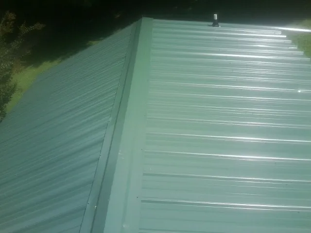 New green metal panels meeting at the ridge of a roof — Flat Roof Repair work by our crew in Oyster Bay