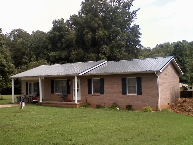 Gray metal roof on a brick ranch house with a side carport in Oyster Bay