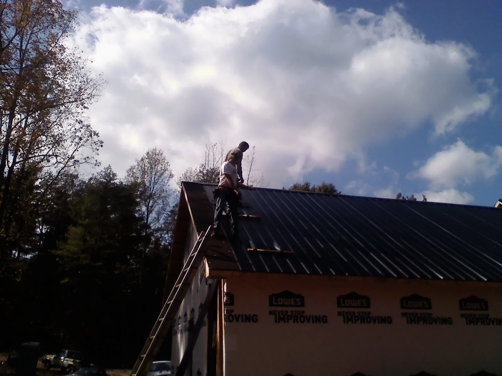 Roofer fastening dark metal panels high against a cloudy sky, from a Roof Inspection job in Oyster Bay