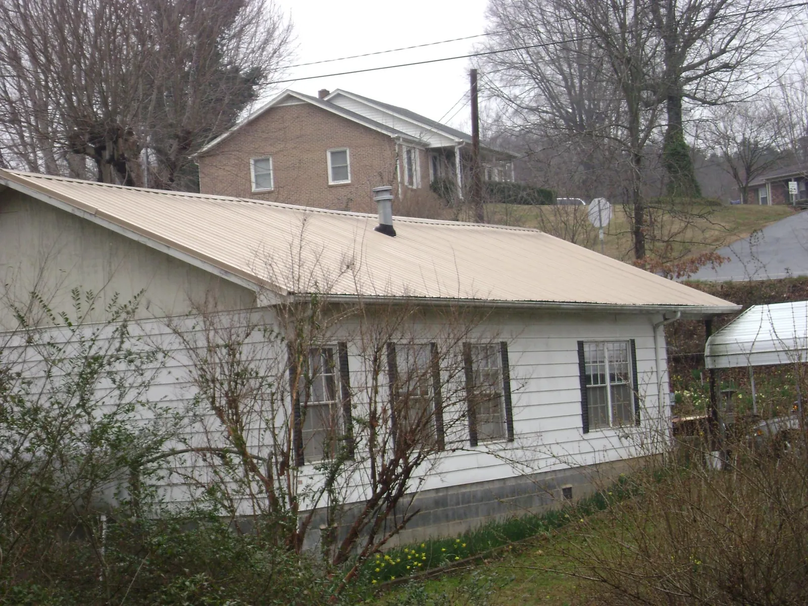 Tan metal roof on a white sided house set into a hillside — Commercial Roofing by Roofing Brothers in Oyster Bay