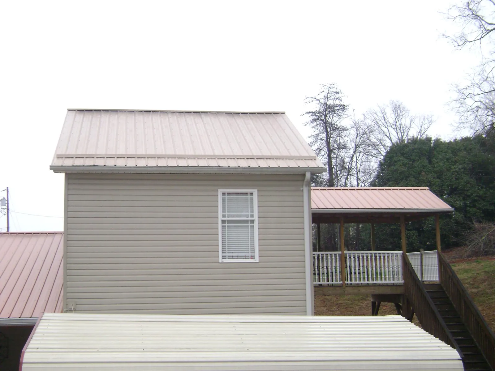 Tan metal roofs on a two story addition and attached porch, from a Roof Replacement job in Oyster Bay